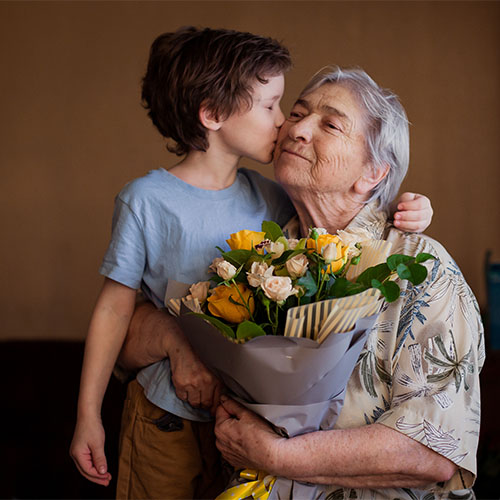 Young boy hugging his Grandma and giving her yellow flowers wrapped in brown paper