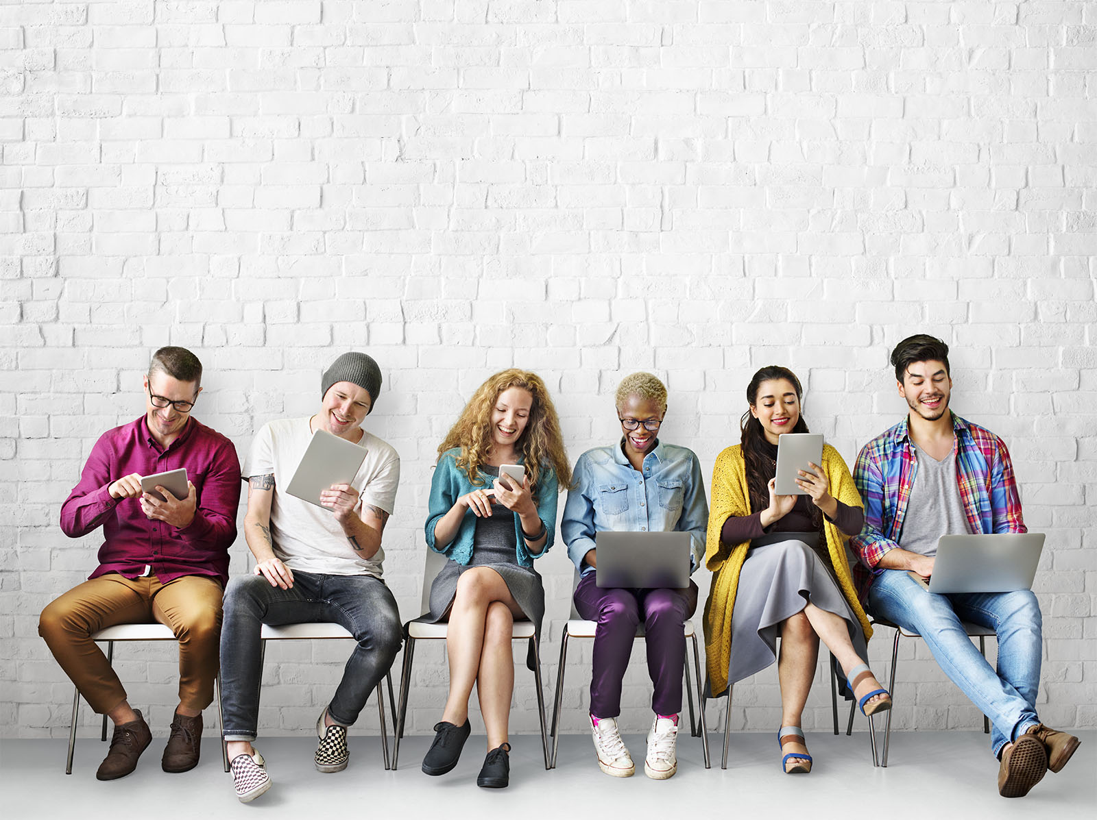 Row of young adults on chairs lined up and all looking at their devices